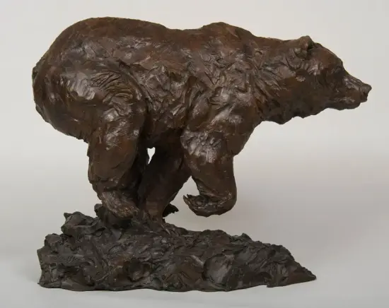 Bronze sculpture of a bear in mid-stride on a rocky base, with a textured surface.
