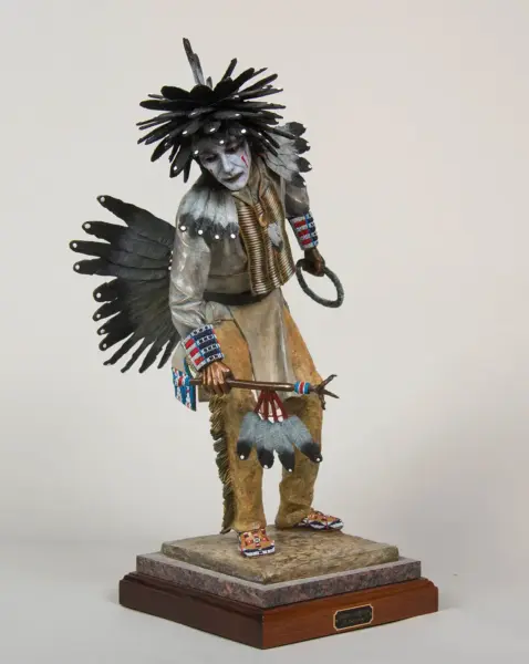 Detailed sculpture of a native figure in ceremonial attire with a black feather headdress, standing on a marble pedestal.