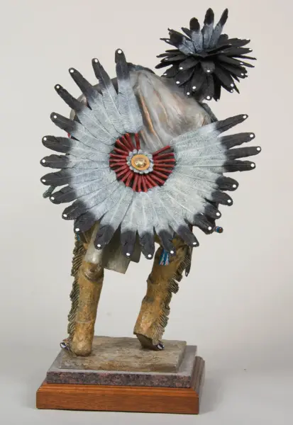 Abstract sculpture of a birdlike figure with a large silver flower with red center on its back, standing on a wooden base.