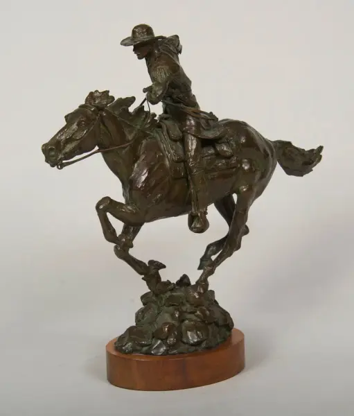 Bronze equestrian statue of a cowboy rider on a rearing horse with a rocky base.