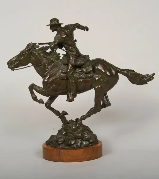 Bronze sculpture of a cowboy riding a rearing horse on a rocky base, mounted on a wooden pedestal.