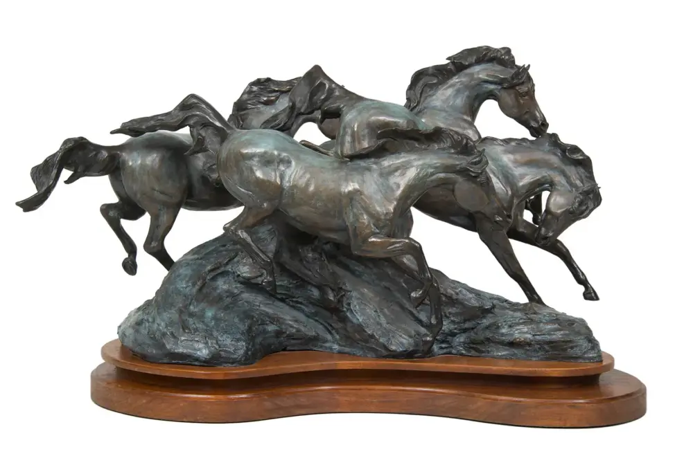 Bronze sculpture of several horses galloping on a rocky pedestal mounted on a wooden base, captured in dynamic motion.