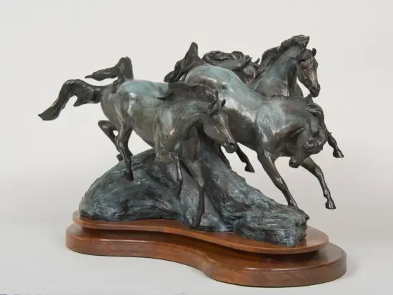 Bronze sculpture of three horses charging over a rocky base on a wooden pedestal
