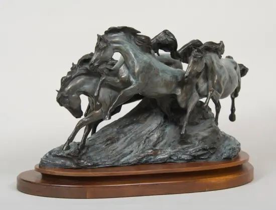 Bronze sculpture of several horses rearing and stirring on a rocky base on a wooden pedestal.