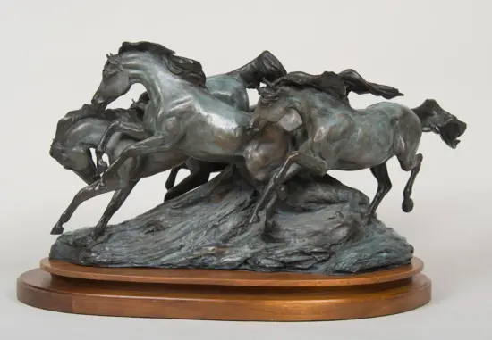 Bronze sculpture of several galloping horses leaping over rocks on a round wooden pedestal