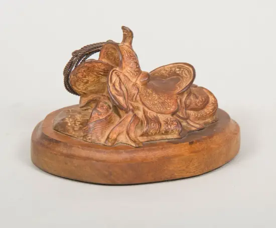 Wooden carved statue of a horse with a detailed saddle and coiled rope on a round wooden base.