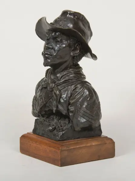 Bronze sculpture bust of a cowboy wearing a hat and neckerchief, mounted on a wooden base.