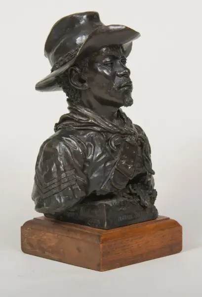 Bronze bust of a man wearing a wide-brimmed hat, mounted on a wooden pedestal.