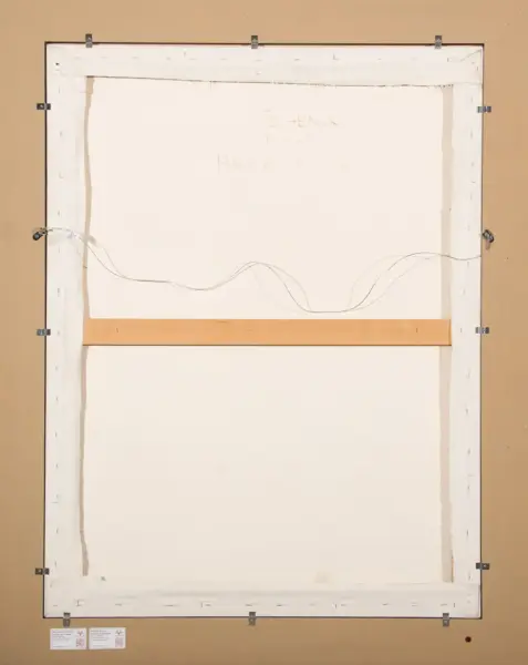 Back of a stretched canvas on a wooden frame with hanging wire and metal staples along the edges; a beige wall surrounds it.