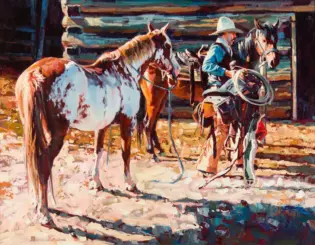 A cowboy in a blue shirt with a white hat stands beside a saddled horse, holding a lasso in a corral with another horse nearby.