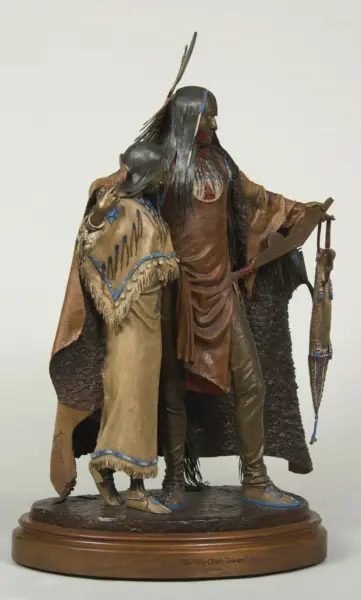 Two Native American figures in buckskin with beadwork and feather adornments, standing on a round wooden display base—an intricate sculpture.
