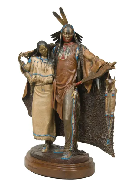 Bronze-toned sculpture of a Native American man in a feathered headdress with a woman beside him, both in fringed beadwork attire on a round pedestal