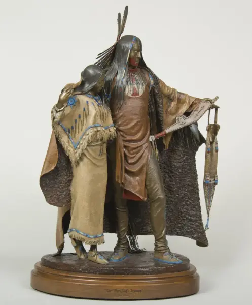 Bronze-toned sculpture of two Native American figures in ceremonial dress on a wooden base, one with a feather headdress and long hair, the other draped in fringed clothing.