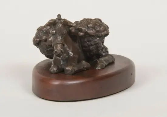 Dark bronze sculpture of a crouching animal on a circular wooden base, with a chunky, textured surface suggesting fur or scales.