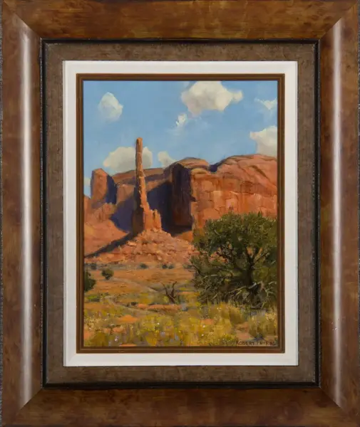 Framed landscape painting of red desert rock formations under a blue sky with scattered clouds and foreground shrubs.