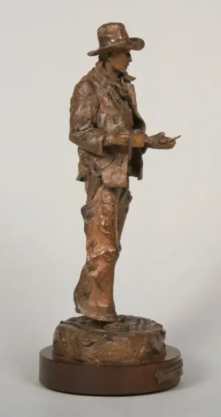 Bronze sculpture of a man in a wide-brimmed hat, wearing a jacket, standing on a round pedestal with a rough textured surface.