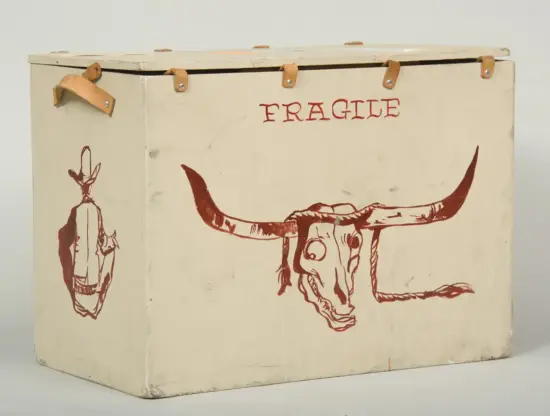 Beige wooden crate marked FRAGILE with a red longhorn skull illustration on the front and a hanging figure drawn on the side.
