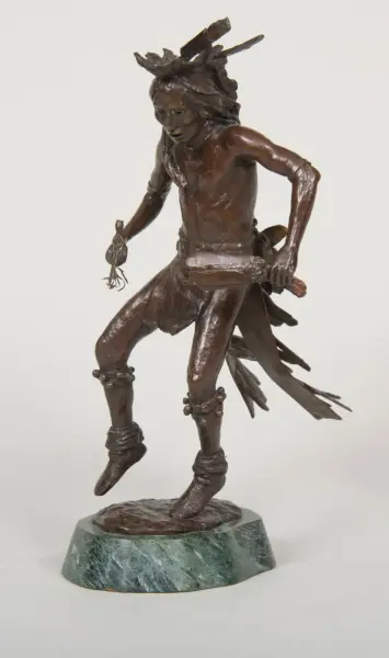Bronze sculpture of a Native American dancer with a feathered headdress, holding a small object, on a green marble base.