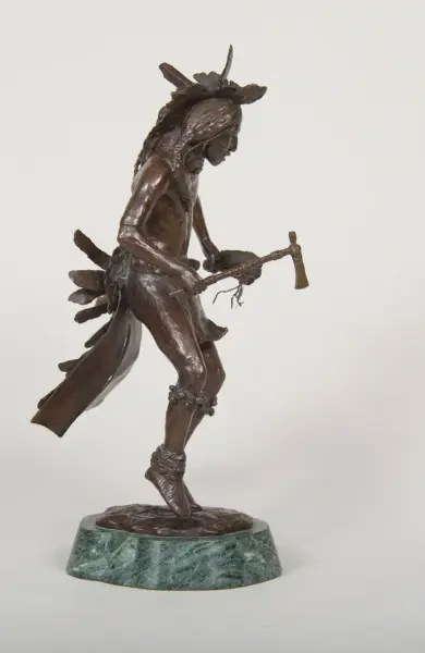 Bronze sculpture of a Native American man in motion, with a feathered headdress, tomahawk in hand, and a green marble base.