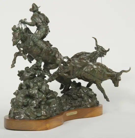 Bronze sculpture of a rider on a rearing horse, with a lasso in hand, mounted on a wooden base with a plaque