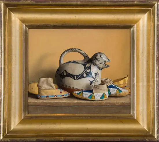Framed still life: a white ceramic teapot with black geometric designs, surrounded by beaded moccasin slippers.