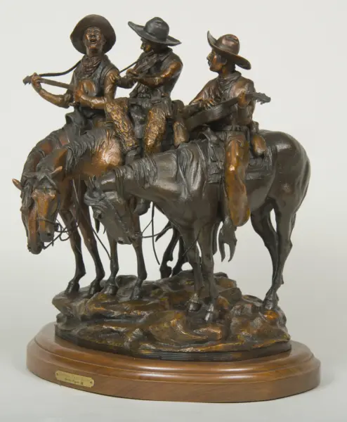 Bronze sculpture of three cowboys on horseback, playing guitars, mounted on a wooden base with a plaque beneath.