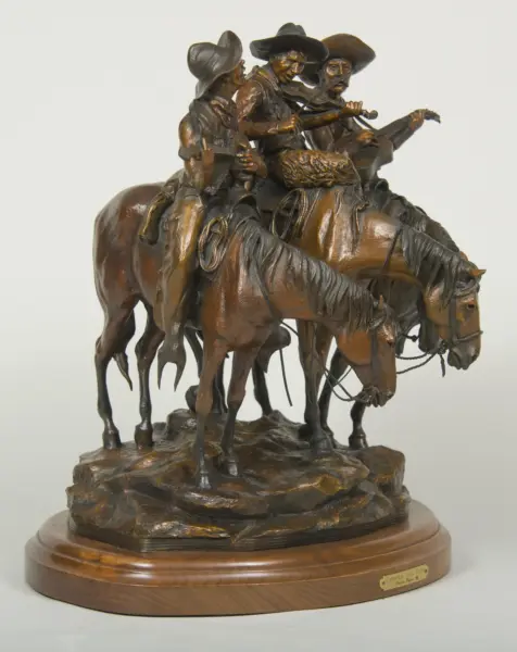 Bronze sculpture of four cowboys on horses gathered on a rocky base with a wooden pedestal beneath them.