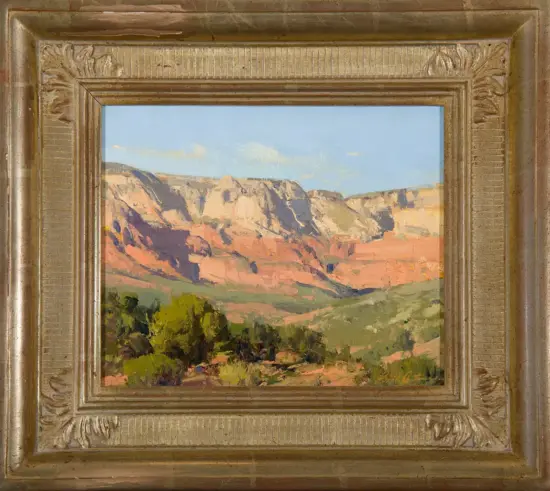 Landscape painting of a canyon with red rock cliffs, blue sky, and green foreground shrubs, housed in an ornate gold frame