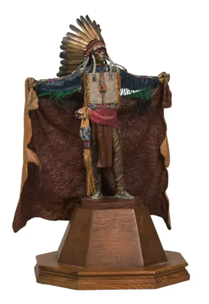 Statue of a Native American chief with a tall feather headdress, outstretched arms, and beaded attire on a wooden pedestal