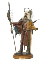 Life-sized statue of a Native American warrior in a feathered headdress, holding a spear and bow on a wooden base.