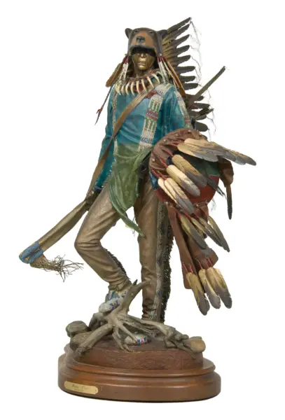 Life-sized sculpture of a Native American warrior in a feathered headdress and beadwork, standing on a wooden pedestal.