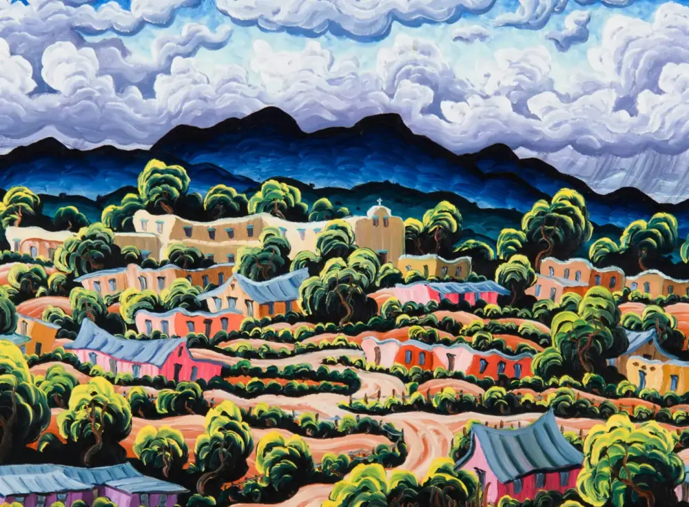Colorful hillside village with warm-toned houses, abundant greenery, and a blue mountain range under a cloudy sky.