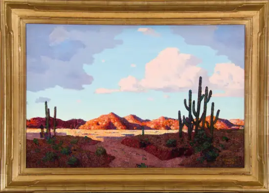 Desert landscape painting with red rocky hills, tall cacti, and a blue sky with fluffy clouds, in a gold ornate frame.