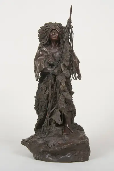 Bronze sculpture of a tall, cloaked figure with a leaf‑like cloak, raised arm holding a spear, on a rocky base.
