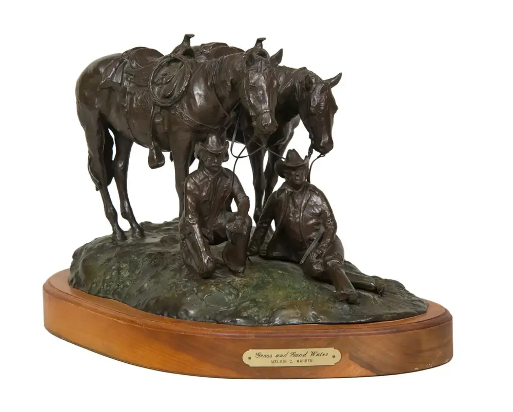 Bronze sculpture of two seated cowboys with horses on a rocky base, mounted on a wooden pedestal. Plaque reads 'Grass and Good Water' by Melvin C. Warren.