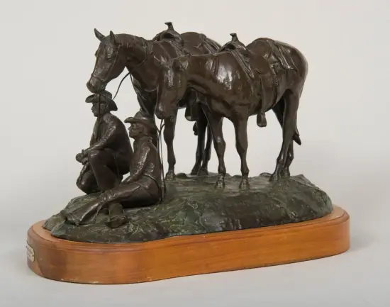 Bronze sculpture of two horses with two seated figures kneeling beside them on a rocky base, mounted on a wooden plinth.