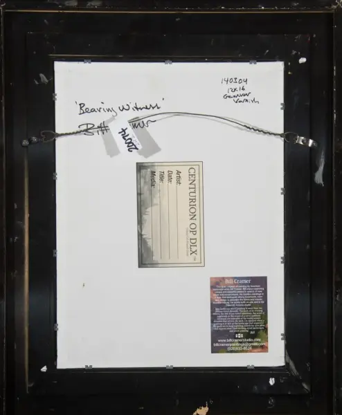Back of framed artwork showing hanging wire, labels, and gallery stickers on white backing board in a black frame surface