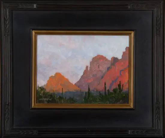 Desert landscape painting: red rock formations at sunset with scrub and cacti in the foreground.