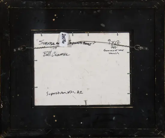 Back of a black framed artwork with a white inner panel, a hanging wire, and handwritten notes taped across it (glimpses of text like 'Sunrise' and 'Superstition Mt AZ').