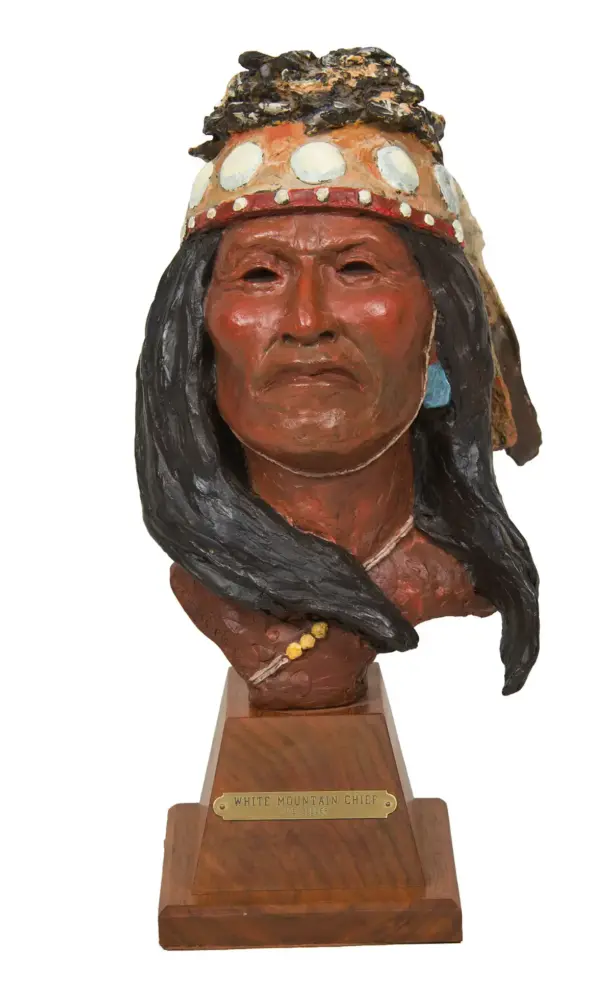 Clay bust sculpture of a Native American chief with a feathered headdress on a wooden pedestal, plaque reads 'White Mountain Chief'