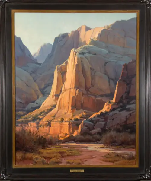 Framed landscape painting of a desert canyon with towering orange rock formations bathed in sunlight.