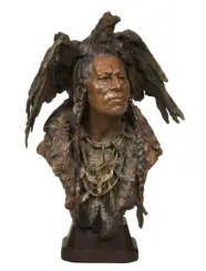 Bronze bust of a Native American figure wearing a feathered headdress and beaded jewelry on a wooden pedestal.