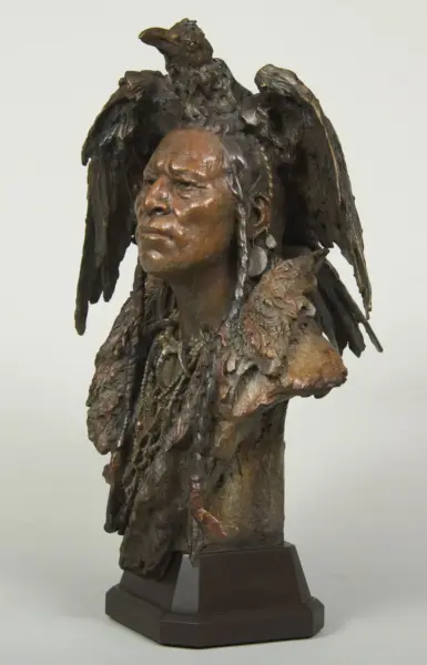 Bronze bust of a person with dark, textured wings draped over the shoulders and a bird perched atop the head, on a dark pedestal.