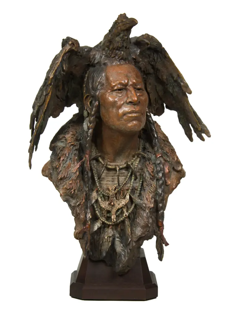 Bronze bust of a Native American figure wearing a feathered headdress and beaded jewelry on a wooden pedestal.