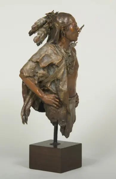 Bronze sculpture of a person with a feathered headdress, wearing tattered clothing, posed on a wooden pedestal base.