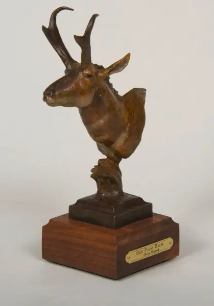 Bronze sculpture of a deer's head with antlers on a wooden pedestal, mounted as a trophy.