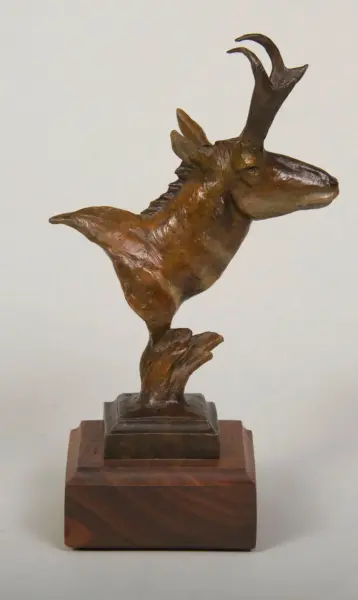 Bronze sculpture of a horned antelope on a wooden pedestal, facing right.