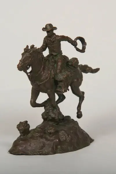 Bronze statue of a cowboy on a rearing horse, raising a lasso in one hand atop a rocky base.