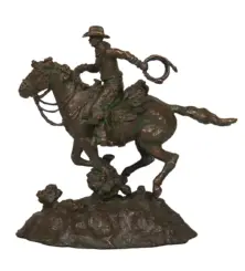 Bronze statue of a cowboy on a bucking horse, lasso in hand, mounted on a rocky base.
