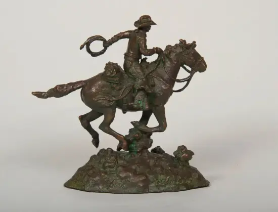Bronze sculpture of a cowboy on a bucking horse, lasso in hand, mounted on a rocky base